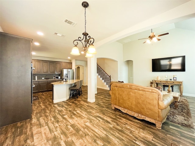 living area with vaulted ceiling, visible vents, arched walkways, and dark wood-type flooring