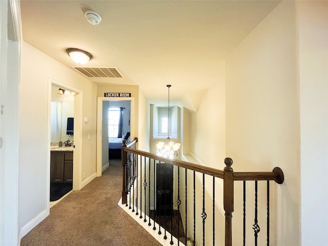 hallway with visible vents, an inviting chandelier, carpet flooring, an upstairs landing, and a sink