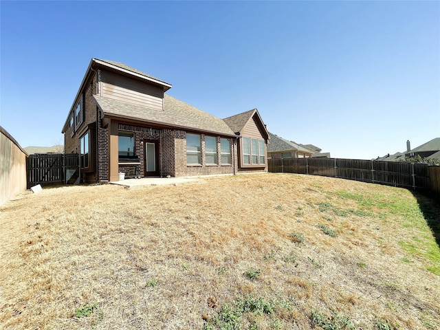 back of property featuring brick siding, a lawn, and a fenced backyard