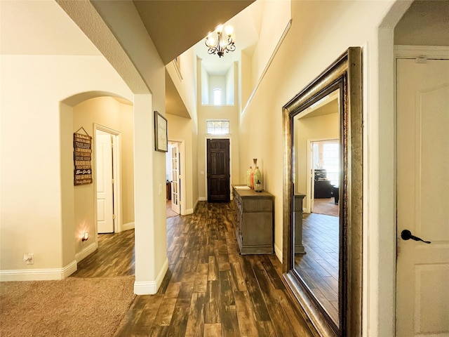 foyer featuring dark wood-style floors, baseboards, arched walkways, and a notable chandelier