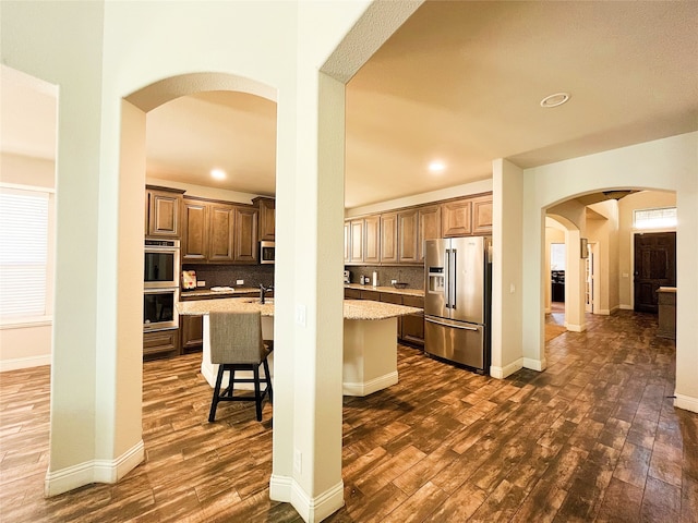 kitchen with stainless steel appliances, arched walkways, dark wood-style flooring, and decorative backsplash