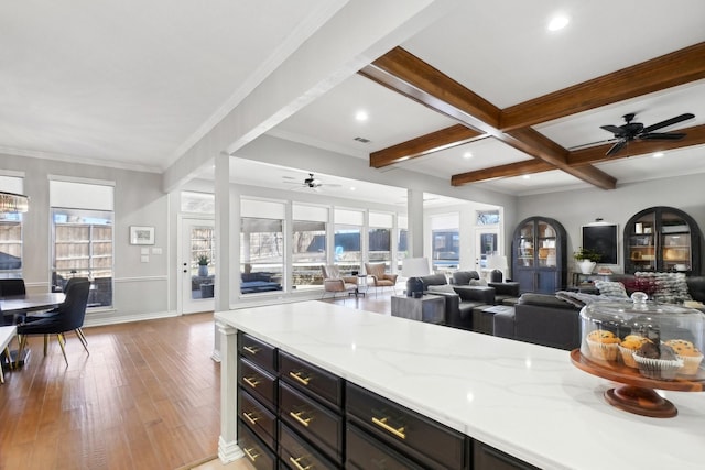 kitchen with light wood-type flooring, beam ceiling, coffered ceiling, open floor plan, and light stone countertops