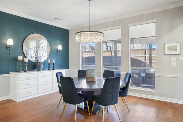 dining area with wood finished floors, baseboards, visible vents, an inviting chandelier, and ornamental molding