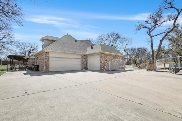 view of side of home with brick siding, an attached garage, driveway, and a gate