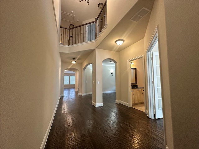 interior space featuring arched walkways, visible vents, a towering ceiling, wood finished floors, and baseboards