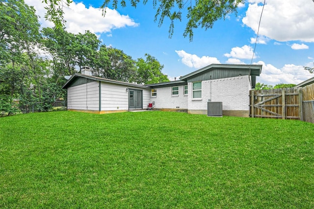 back of house featuring fence, a yard, central AC, a chimney, and brick siding