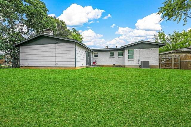 rear view of property featuring fence, a yard, cooling unit, brick siding, and a chimney