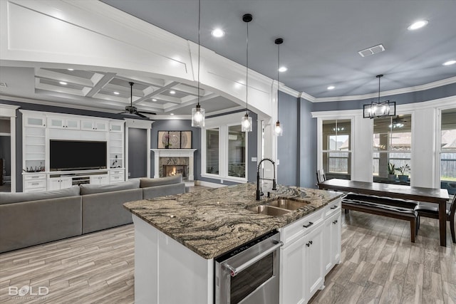 kitchen with a sink, a warm lit fireplace, ornamental molding, and ceiling fan with notable chandelier