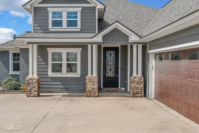 doorway to property featuring concrete driveway, a shingled roof, and a garage