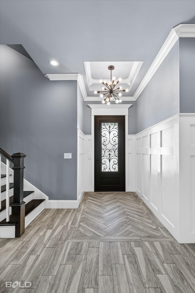 foyer entrance with ornamental molding, wainscoting, a decorative wall, a chandelier, and stairs