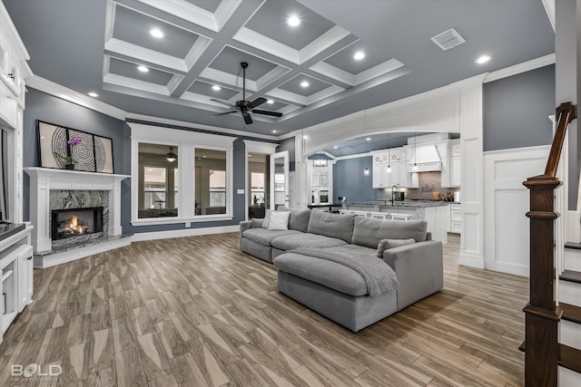 living area with visible vents, coffered ceiling, a high end fireplace, ornamental molding, and beamed ceiling