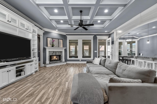 living room featuring light wood-type flooring, coffered ceiling, ornamental molding, and ceiling fan with notable chandelier