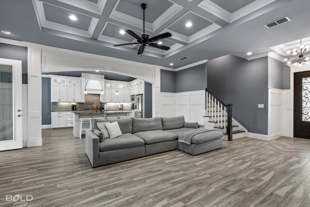 living area featuring visible vents, a high ceiling, crown molding, light wood finished floors, and stairs