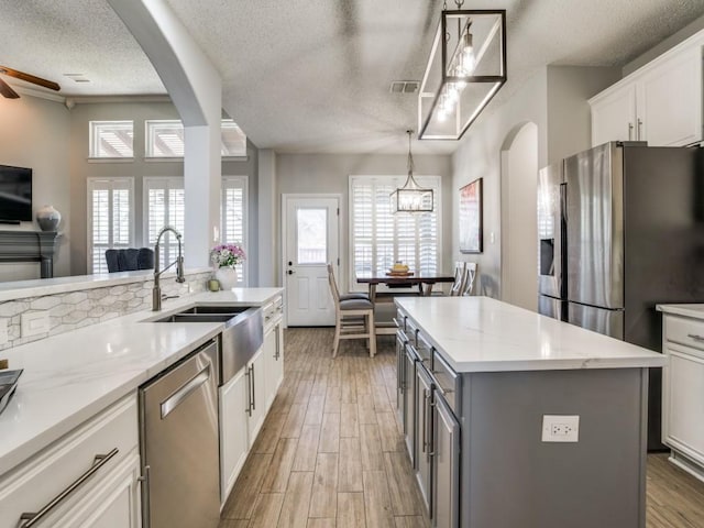 kitchen featuring stainless steel appliances, arched walkways, gray cabinets, and a sink