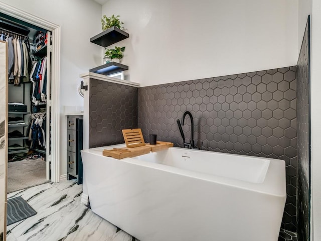 bathroom with tile walls, marble finish floor, a freestanding bath, and a spacious closet