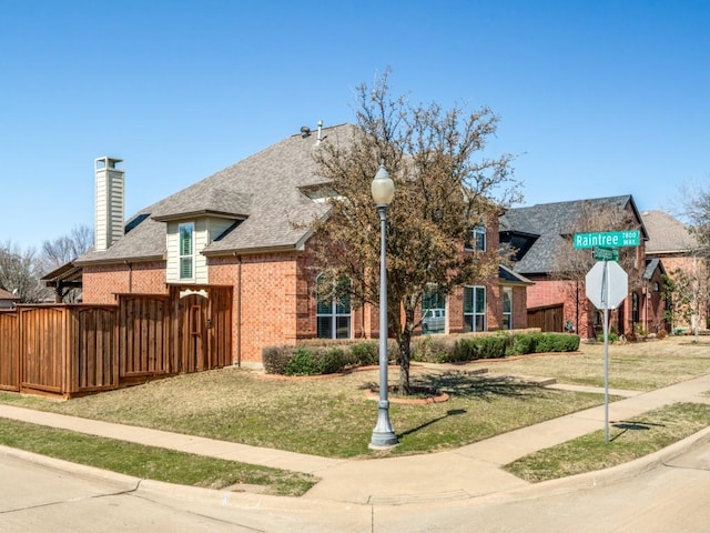 view of front facade featuring a shingled roof, a front yard, a chimney, and brick siding