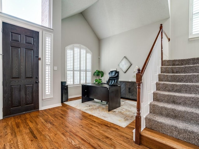 foyer with high vaulted ceiling, stairway, baseboards, and wood finished floors