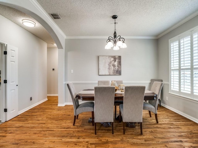 dining room with arched walkways, wood finished floors, visible vents, ornamental molding, and an inviting chandelier