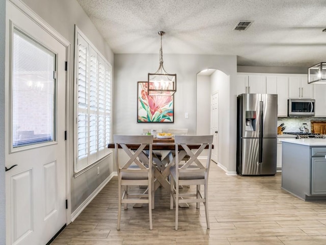 dining space with light wood finished floors, visible vents, arched walkways, and baseboards