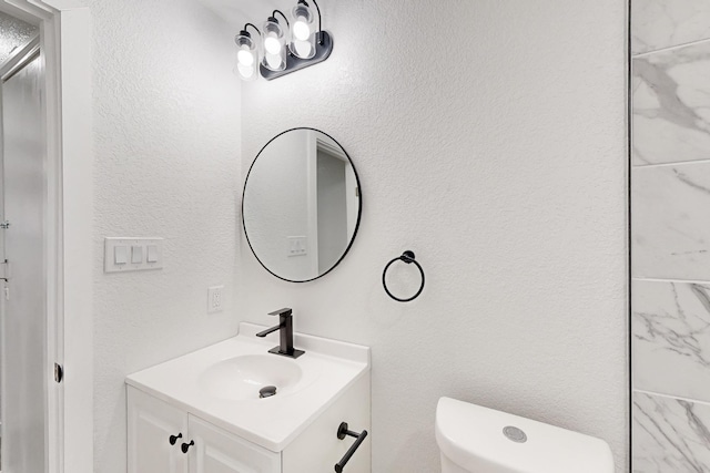 bathroom with toilet, a textured wall, and vanity