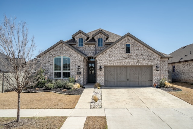 french country inspired facade featuring driveway, brick siding, roof with shingles, and an attached garage