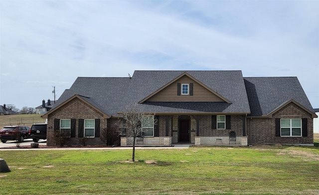 view of front of home featuring brick siding, roof with shingles, and a front yard