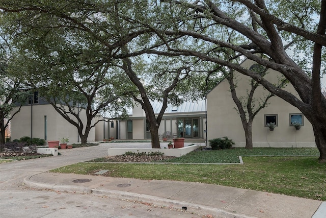 view of front of property featuring a front yard, a standing seam roof, metal roof, and stucco siding