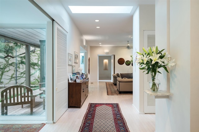 corridor with a skylight, expansive windows, light wood finished floors, and recessed lighting