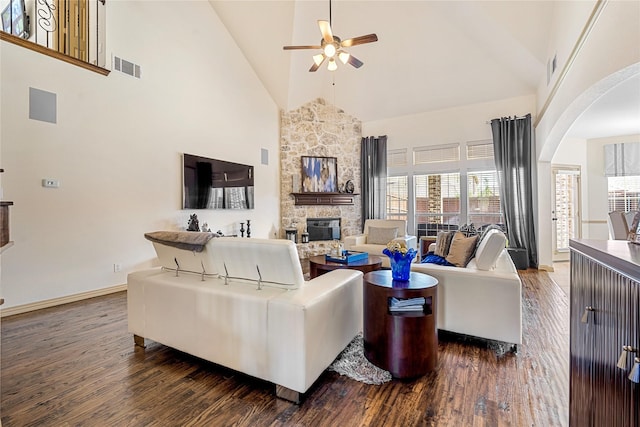 living room with visible vents, arched walkways, dark wood-type flooring, and a stone fireplace