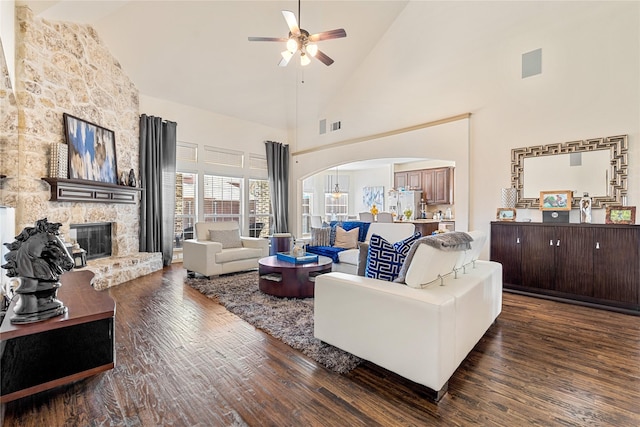 living area featuring arched walkways, ceiling fan, a stone fireplace, high vaulted ceiling, and wood finished floors