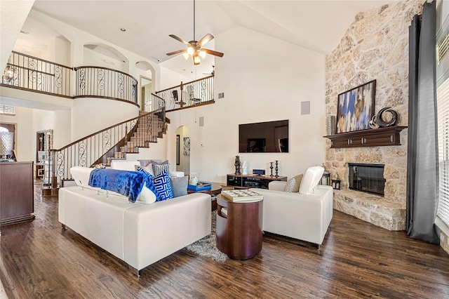 living room with ceiling fan, a stone fireplace, visible vents, stairs, and dark wood finished floors