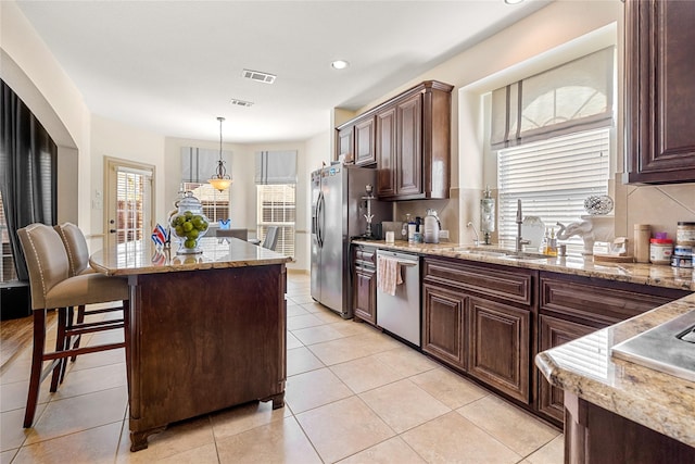 kitchen with visible vents, a kitchen island, appliances with stainless steel finishes, light stone counters, and a sink