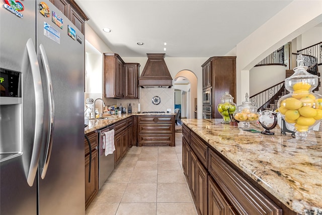 kitchen featuring light tile patterned flooring, a sink, appliances with stainless steel finishes, custom exhaust hood, and tasteful backsplash