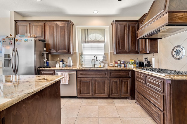 kitchen featuring light stone counters, custom exhaust hood, stainless steel appliances, a sink, and light tile patterned flooring