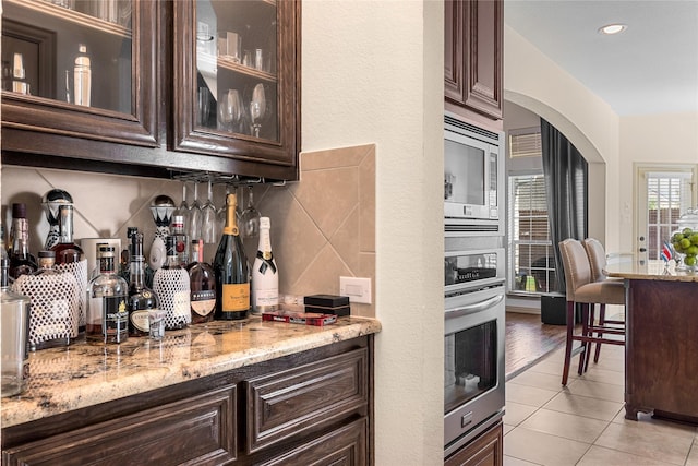 kitchen with stainless steel appliances, light stone counters, dark brown cabinets, and light tile patterned floors