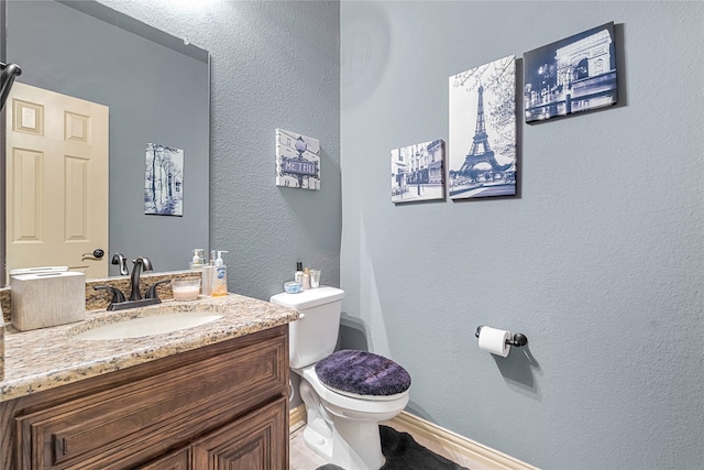 half bathroom with a textured wall, vanity, and toilet