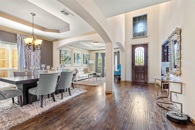 foyer entrance featuring a tray ceiling, arched walkways, wood-type flooring, an inviting chandelier, and baseboards