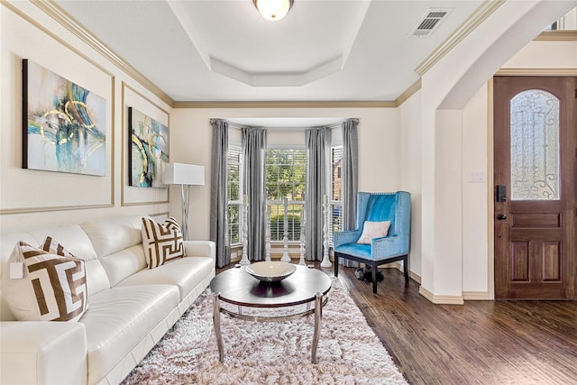 living room featuring arched walkways, dark wood-style flooring, a tray ceiling, visible vents, and ornamental molding