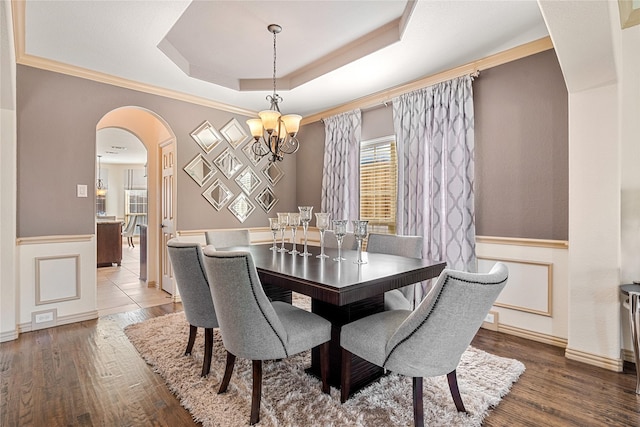 dining area featuring arched walkways, a raised ceiling, a wainscoted wall, and wood finished floors