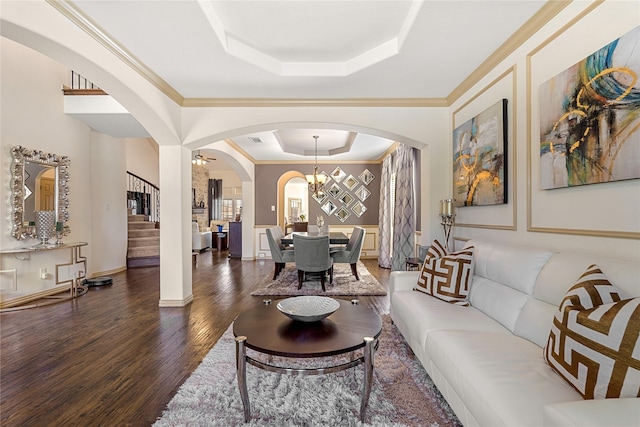 living area featuring a notable chandelier, wood finished floors, stairs, ornamental molding, and a tray ceiling