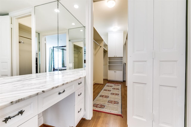 bathroom with a walk in closet, vanity, recessed lighting, and wood finished floors