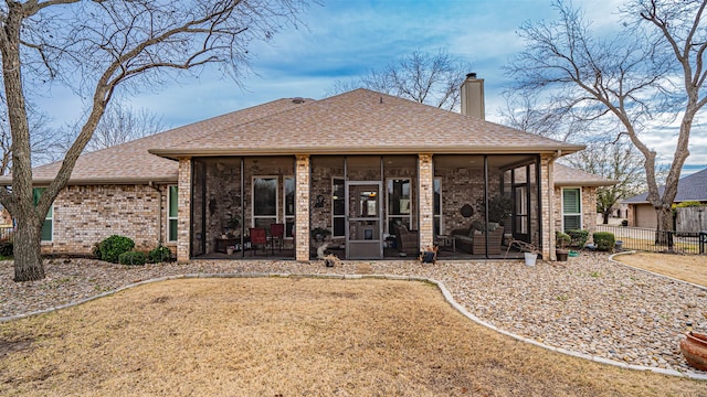 rear view of house with a shingled roof, a sunroom, a chimney, fence, and brick siding