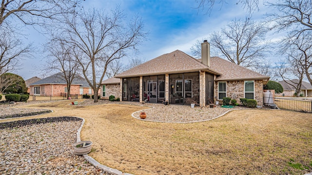 back of house featuring brick siding, a yard, a chimney, a sunroom, and fence