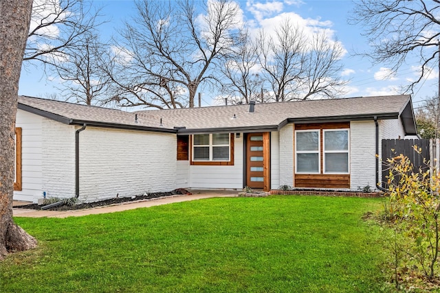 view of front of house with a shingled roof, a front yard, fence, and brick siding