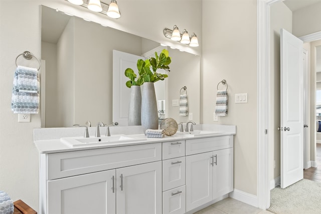 ensuite bathroom with tile patterned flooring, a sink, baseboards, and double vanity