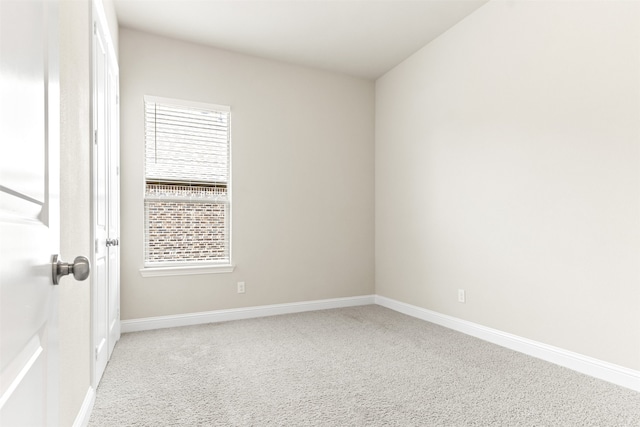 spare room featuring light colored carpet and baseboards