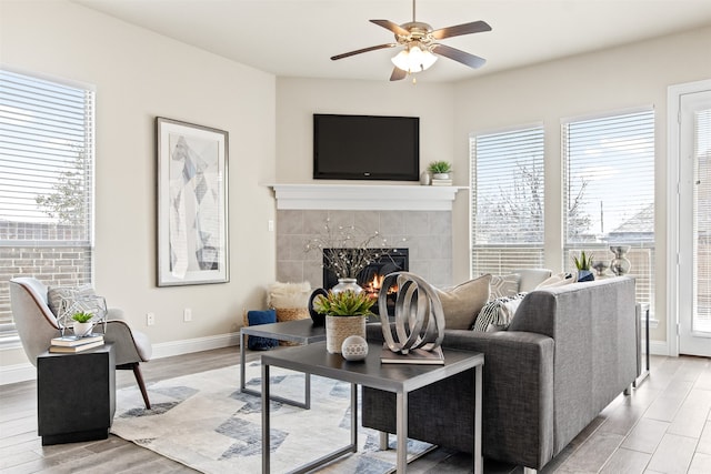 living room featuring light wood-type flooring, ceiling fan, baseboards, and a tile fireplace