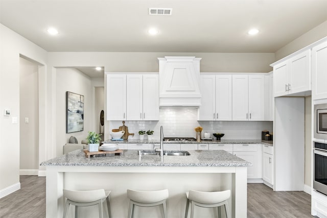 kitchen with light wood finished floors, a sink, visible vents, and decorative backsplash