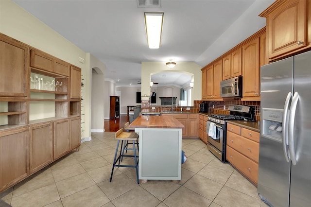 kitchen with light tile patterned floors, arched walkways, stainless steel appliances, butcher block counters, and a kitchen breakfast bar