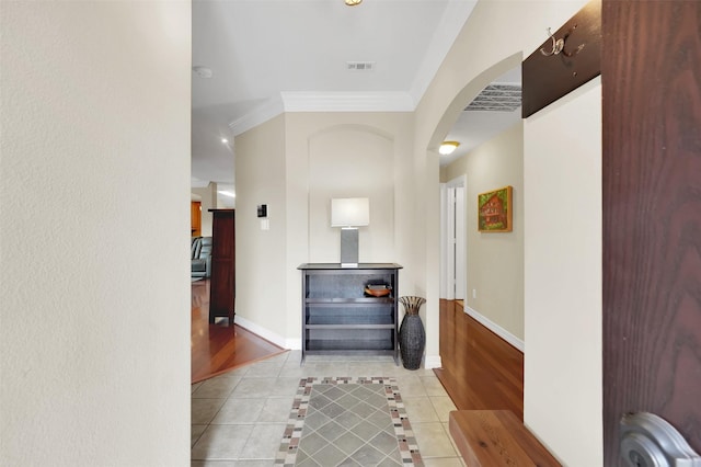 corridor featuring arched walkways, tile patterned flooring, visible vents, baseboards, and crown molding